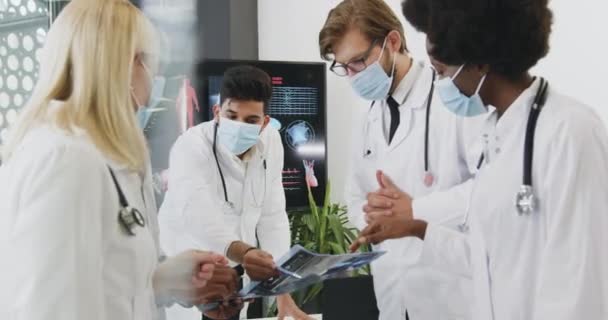 Atraente confiante cvalified mestiço trabalhadores médicos em máscaras analisando imagem de raios-X durante reunião na sala de reuniões, conceito de pandemia covid-19 — Vídeo de Stock