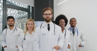 İyi görünümlü, başarılı, kendine güvenen bir grup doktorun portresi toplantı odasında kameranın önünde duruyor.