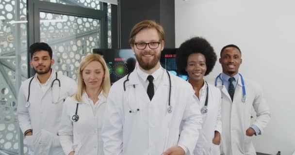 Mutlu yüzlü kameraya bakan beyaz üniformalı başarılı erkek ve kadın doktorların tıbbi portresi. — Stok video