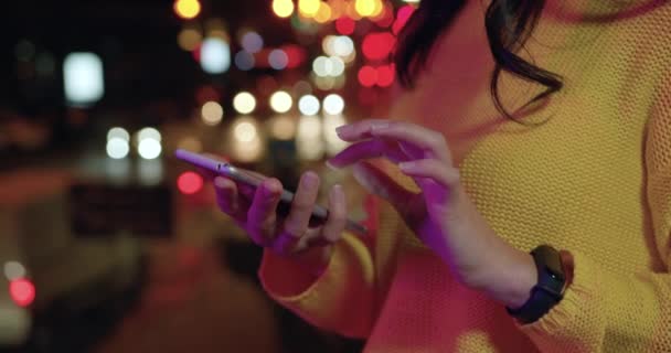 Vue de face des mains de femmes qui utilisent son smartphone le soir parmi les lumières de la ville nocturne — Video