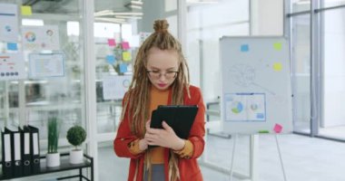 Modern ofis odasındaki tablet bilgisayarında çalışan şık kıyafetler ve gözlüklü, konsantre olmuş, genç ve güzel bir kadının portresi.