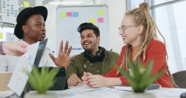 Primer plano de simpáticos compañeros de equipo profesionales multiétnicos experimentados y confiados que consultan sobre detalles de un proyecto conjunto en una moderna sala de oficinas de vidrio — Vídeos de Stock