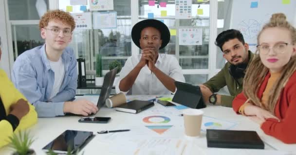 Attractive joyful confident stylish young multiracial office workers sitting at boardroom table and looking into camera and showing gesture "well done"with hands ,slow motion — Stock Video