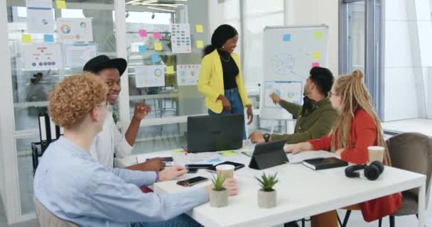 Conceito de trabalho de escritório onde simpática positiva bem sucedida motivado equipe diversificada discutir estratégia de projeto conjunto usando infográficos na parede de vidro na sala de escritório — Vídeo de Stock