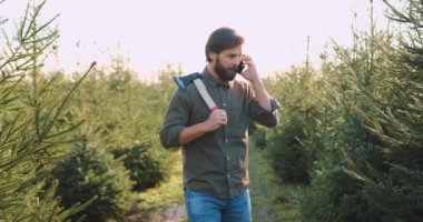 Elinde balta olan yakışıklı, pozitif sakallı bir adamın yakınına. Ağaçların arasında ağaçların arasında yürüyor ve telefonla konuşuyor.