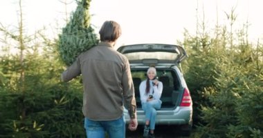 Yakışıklı, gülümseyen, sakallı, güzel karısına köknar ağacı getiren, arabanın bagajında oturan, termostan çay içen ve köknar ağaçları arasında cep telefonunu kullanan yakışıklı adam.