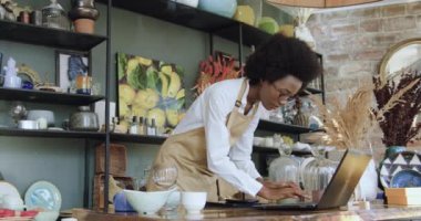 Kendi el yapımı hediyelik eşya dükkanından fotoğraf çeken ve internet pazarı için bilgisayara fotoğraf yükleyen Afro-Amerikan kadın işçinin kasıtlı portresi.