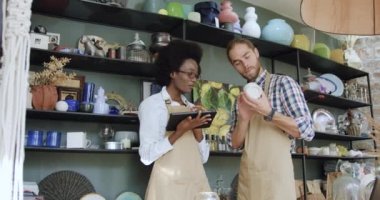 Çekici gülümseme deneyimli genç melez ırk satıcıları el yapımı güzel bir hediyelik eşya dükkanında birlikte çalışıyorlar ve hasarları kontrol ediyorlar.