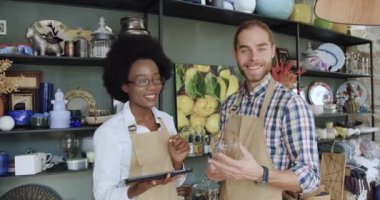 Güzel bir hediyelik eşya dükkanında çalışırken kameraya şanslı yüzlerle poz veren önlüklü, neşeli, dost canlısı, karışık ırk satıcılarının ön görüntüsü.