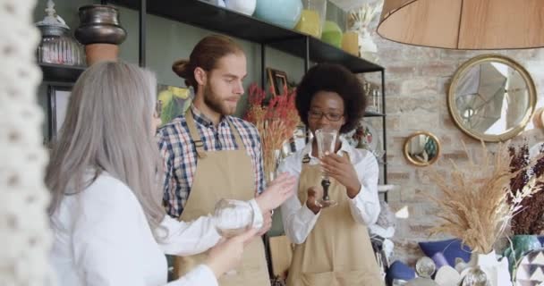 Likable satisfied mixed race sellers proposing wine glasses for beautiful mature woman in cozy small gift shop — Stock Video