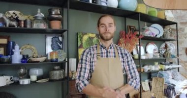 Çekici, gülümseyen, kendine güvenen, sakallı bir adamın ön görüntüsü. Güzel bir hediyelik eşya dükkanında kollarını kavuşturarak kameraya poz veriyor.