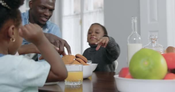 Atraente sorrindo feliz família afro-americana despreocupada sentada à mesa de jantar e comer deliciosos biscoitos, conceito de família, 4k — Vídeo de Stock