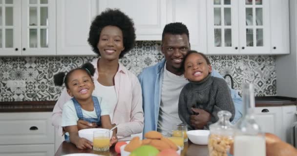 Retrato de adorable sonriente feliz despreocupada familia de piel negra que se sienta en la mesa durante el desayuno y mirando a la cámara con caras satisfechas, cámara lenta — Vídeos de Stock