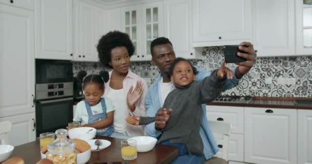 Adorable jeune famille moderne souriante et heureuse avec des enfants faisant du selfie au téléphone assis à la table de la cuisine pendant le petit déjeuner, gros plan, ralenti — Video