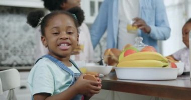 Güzel, mutlu, küçük, siyah tenli, tatlı kurabiyelerle yemek masasında oturan ve kameraya samimi bir gülümsemeyle bakan kız.