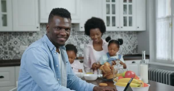 Retrato de atractivo hombre de piel negra despreocupado positivo de 35 años que posa en la cámara en la cocina contemporánea cerca de su hermosa esposa y dos hijas pequeñas, 4k — Vídeos de Stock