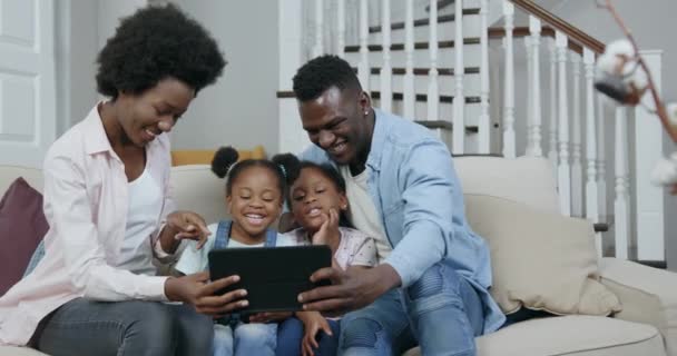 Retrato de bonita sonriente feliz joven familia de piel negra moderna con niños que se relajan en un cómodo sofá en la sala de estar y el uso de la tableta PC para revisar videos divertidos, 4k — Vídeo de stock