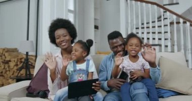 Kameranın önündeki koltukta oturan ve herkese merhaba demek için el sallayan sevimli, mutlu, modern Afro-Amerikan ailesinin portresi.