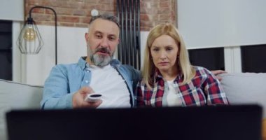 Güzel görünümlü, heyecanlı, dizüstü bilgisayarda film izleyen ve ekrandaki korkunç sahneden gözlerini ve ağızlarını kapatan yetişkin çiftin ön görüntüsü.