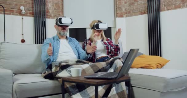 Portret van goed uitziende serieus zelfverzekerde volwassen echtpaar die samen zitten op de bank thuis en werken op virtueel scherm in speciale 3d bril — Stockvideo