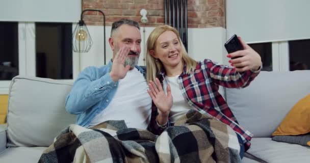 Aangenaam tevreden getrouwd volwassen paar ontspannen op zachte binnenlandse bank in de avond tijd en het maken van selfie op mobiel, familie concept, close-up — Stockvideo