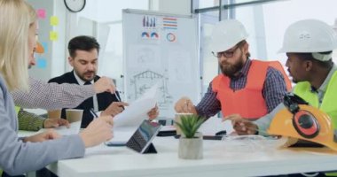 Çekici, profesyonel, çok ırklı mühendisler ve onların atraktif sakallı müşterileri ya da ana yöneticileri ofis odasında toplantı sırasında proje inşaatı hakkında fikir alışverişinde bulunuyorlar.