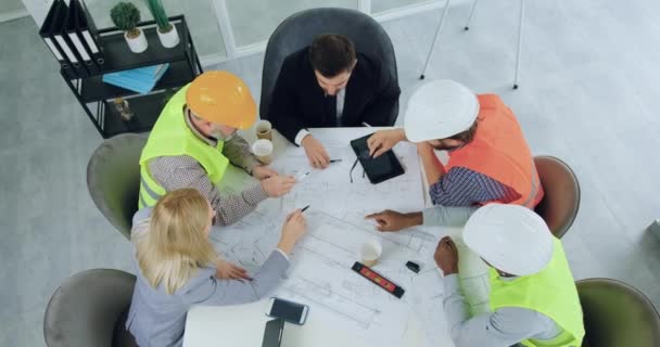 Visão superior de boa aparência positiva experiente equipe multirracial de engenheiros e seus gerentes masculinos e femininos fazendo gesto de unidade com as mãos e levantou-os durante o trabalho conjunto sobre a construção — Vídeo de Stock