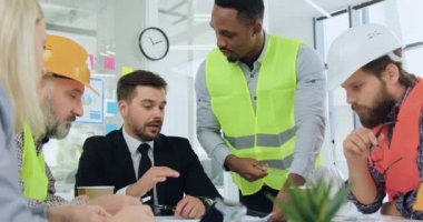 İyi görünümlü, kendine güvenen, siyah derili bir mühendis, çalışan ekibin diğer üyeleriyle görüşmesi sırasında ciddi derecede yetenekli sakallı yöneticisine bina planının detaylarını anlatıyor.