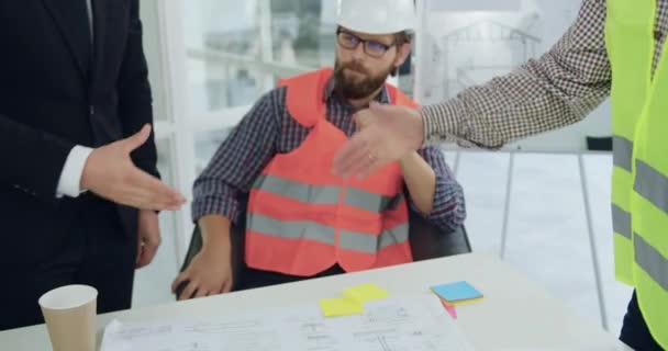 Homem confiante desconhecido em terno handshaking com engenheiro experiente profissional em colete durante reunião na sala de reuniões sobre projeto de construção conjunta — Vídeo de Stock