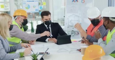 İyi görünümlü, profesyonel, melez, maskeli mühendislerin toplantı sırasında kendine güvenen patronla detaylar hakkında konuştuğu Covid-19 terimleriyle çalışın.