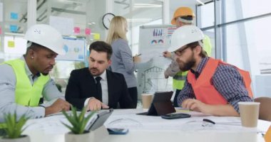 Ofis odasındaki toplantı sırasında ortak inşaat projesi üzerine beyin fırtınası yapan erkek ve kadın mühendislerden oluşan iyi görünümlü profesyonel bir ekibin portresi.