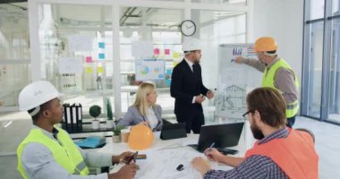 İnşaat endüstrisi konsepti. İyi görünümlü profesyonel mühendisler ve ana yöneticilerden oluşan çok ırklı bir ekip toplantı odasında toplanıyor ve ortak inşaat projesinin detaylarını tartışıyorlar.