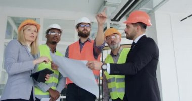 İnşaat alanındaki müşterilerle planlama detaylarını tartışan iyi görünümlü, çok ırklı mühendislerin portresi.