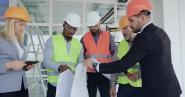 Çekici, yetenekli, kendine güvenen, karışık ırk mühendisleri ya da inşaatçıları ve müşterilerinin ön görüntüsü. İnşaat alanındaki planların detaylarını kontrol ediyorlar.