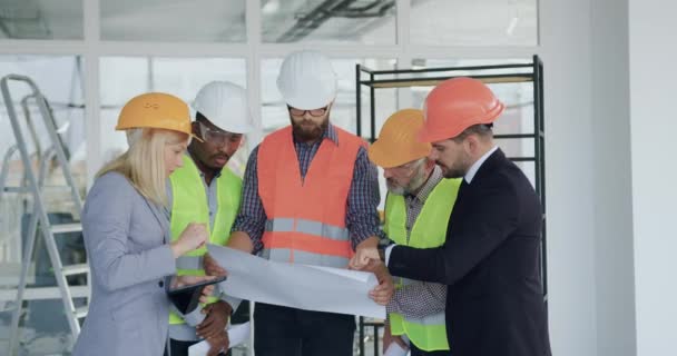 Equipe diversificada altamente qualificada e confiável de empreiteiros que inspecionam novos edifícios com seus clientes concentrados e revisam o plano juntos — Vídeo de Stock