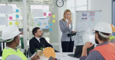 Baya kendine güvenen sarışın bir bayan yönetici, yönetim kurulundaki toplantı sırasında, inşaat endüstrisi konseptini oluşturan üst düzey profesyonel çeşitli inşaatçılara iş talimatları veriyor.