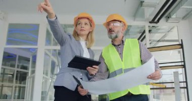 Kasklı teftiş evinde ya da ofisinde profesyonel sakallı müteahhitle birlikte güzel yetenekli sarışın bayan yönetici ve tüm detayları tablet planına göre karşılaştırmak.