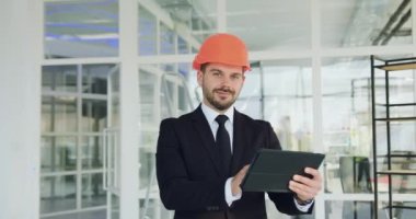 Yakışıklı gülümseyen, başarılı, yüksek yetenekli, sakallı inşaat şirketinin CEO 'su tamamlanmamış ofis binasını incelerken kameraya tablet bilgisayarla poz veriyor.