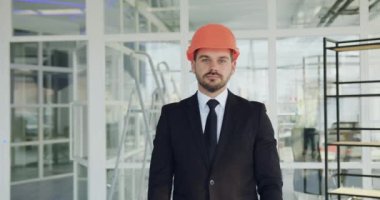 Yakışıklı gülümseyen başarılı sakallı mühendis yarım kalmış ofis binasında kollarını kavuşturarak kameraya poz veriyor.