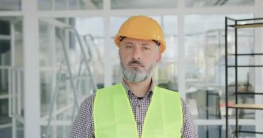 İyi görünümlü mutlu profesyonel sakallı müteahhit ya da özel üniformalı mühendis portresi yeni inşa edilmiş ofiste çapraz kollarla poz veriyor.
