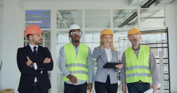 여러 연령의 다양 한 청부업자들과 함께 미완성 사무실 건물을 조사하고 계획을 논의하는 고급 모자를 쓴 남녀 매력적 인 기술을 가진 두 남녀 고객들 — 비디오
