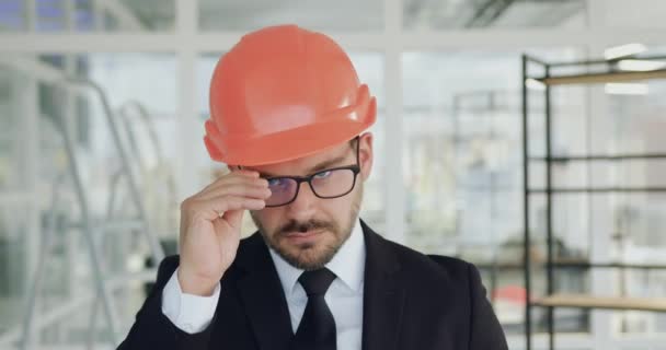 Portret atrakcyjnego doświadczonego w dobrym nastroju brodatego inżyniera w twardej czapce, który zdejmuje okulary i patrzy w kamerę z pewną twarzą — Wideo stockowe