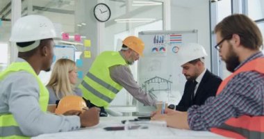 Sevimli profesyonel özgüvenli mühendis ve şeflerden oluşan çok ırklı bir ekip toplantı odasında brifing sırasında hazır bina çizimlerini gözden geçiriyorlar.