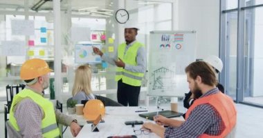 Çekici özgüvenli Afro-Amerikan mühendisi toplantı odasında diğer mimar ekibi üyeleri ve müşterilerin önünde rapor veriyor.