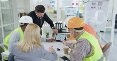 İyi görünümlü, kendine güvenen, inşaat endüstrisi uzmanlarından oluşan çeşitli bir ekip bir toplantı düzenliyor ve tablet bilgisayarına resmedilmiş çizim ile bakarken ortak inşa projesinin detaylarını tartışıyorlar.