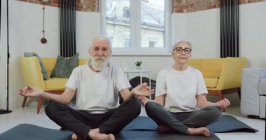 İyi görünümlü, kendine güveni tam, spor giyimli olgun bir çiftin evinde yoga minderlerinde yan yana oturdukları sırada.