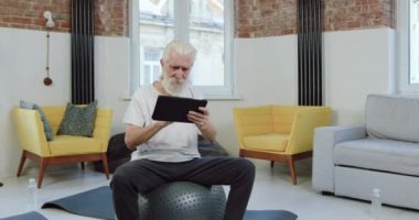 Spor giyimli çekici, konsantre sakallı bir adamın portresi evde spor salonunda oturuyor ve tablet cihaz arama dersleri alıyor.