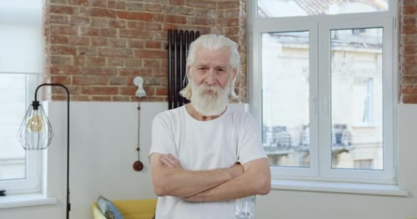 Sympatický sebevědomý starší vousatý muž s vrásčitým obličejem v domácím oblečení pózuje na kameře v současném bytě — Stock video