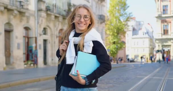 Adorável alegre satisfeito jovem mulher moderna em roupas da moda e óculos desfrutando de seu passeio na cidade com bela arquitetura, vista frontal — Vídeo de Stock