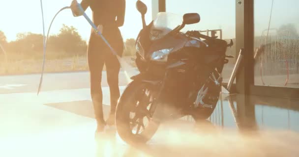 Jovem morena na moda alegre provável em roupas pretas lavando sua moto preta legal na estação de autoatendimento com tubo de água de alta pressão no pôr do sol — Vídeo de Stock
